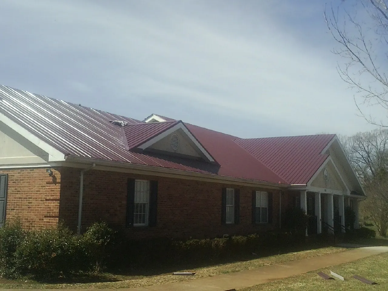 Red metal roof with gabled entries on a long brick building, from a Hail Damage Roof Repair job in Sevierville