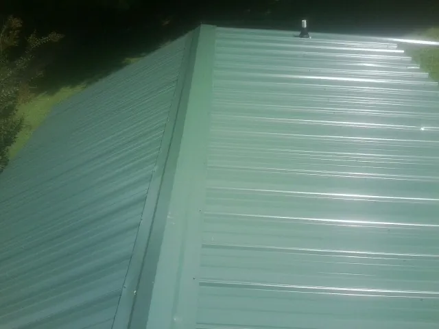 New green metal panels meeting at the ridge of a roof — Flat Roof Repair work by our crew in Sevierville