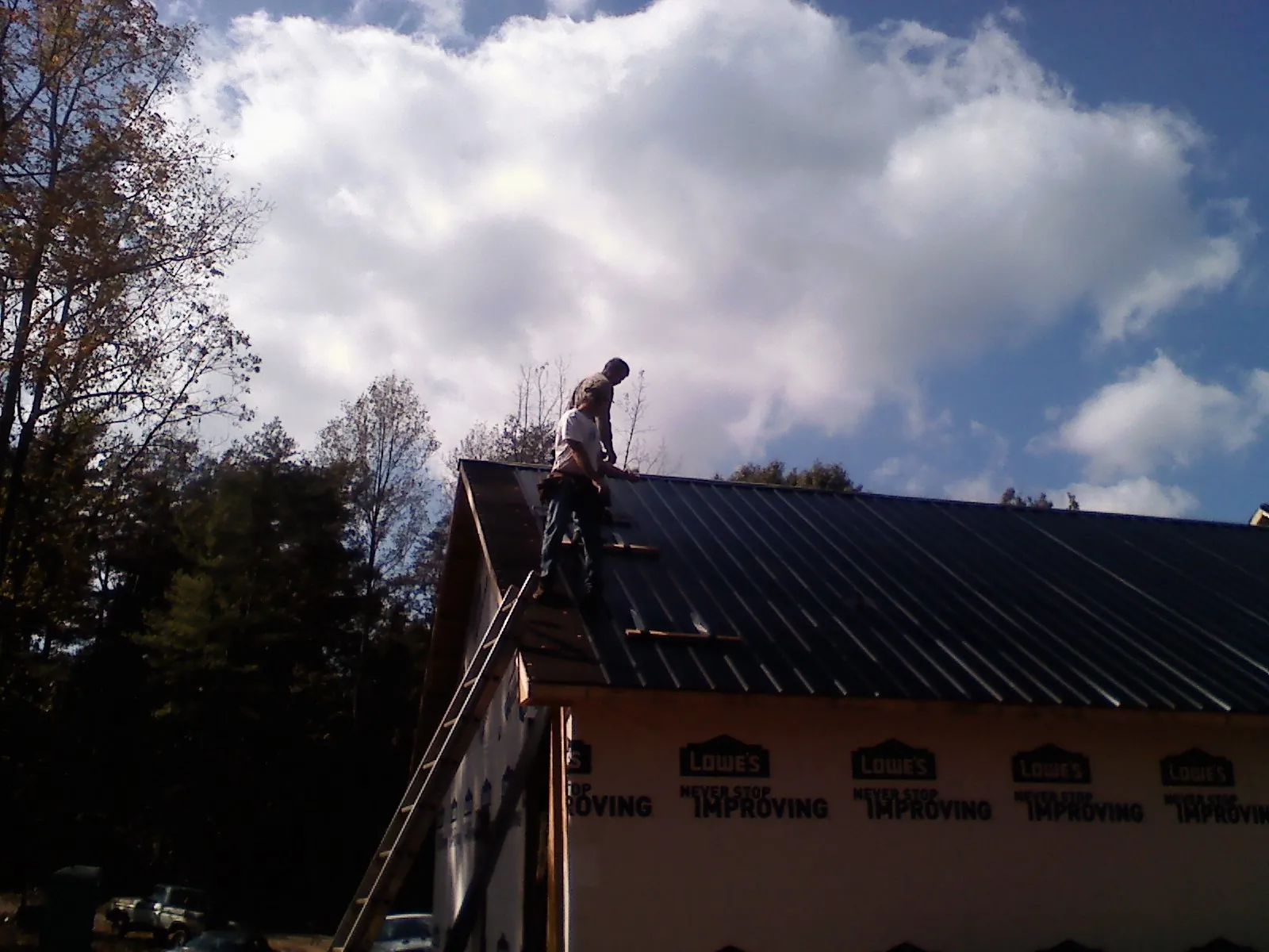Roofer fastening dark metal panels high against a cloudy sky, from a Roof Inspection job in Sevierville