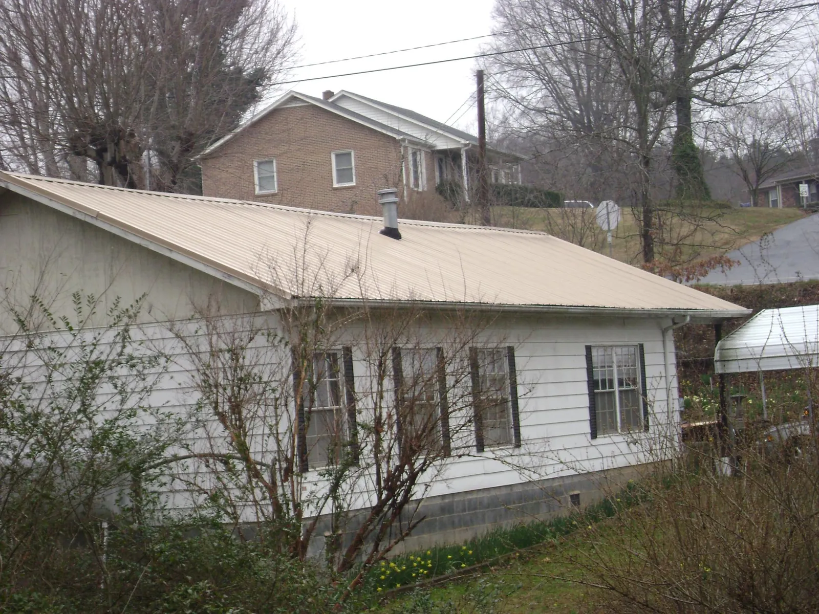 Tan metal roof on a white sided house set into a hillside — Commercial Roofing by Roofing Brothers in Sevierville
